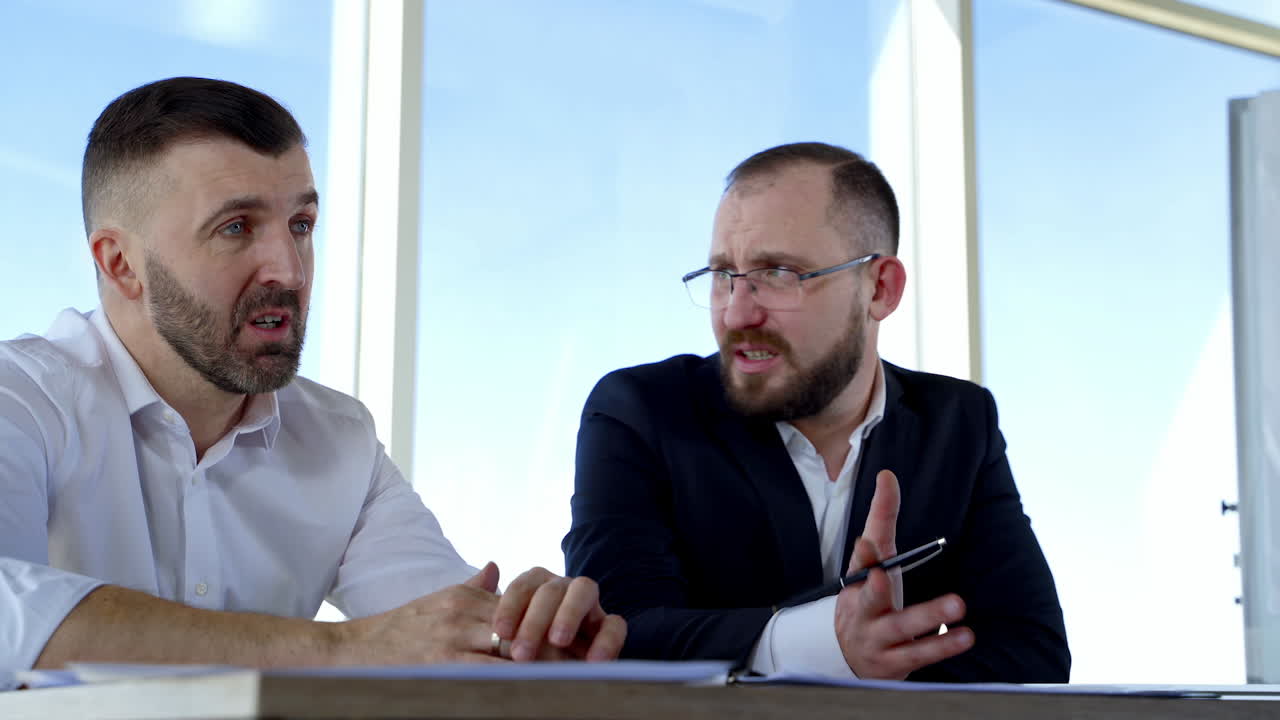 Portrait of two businessmen talking in office. Serious partners discussing business strategy indoors on window background at daytime. Business concept.
