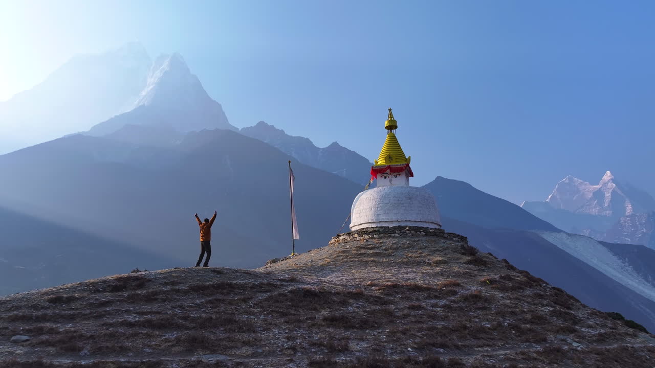 Wide drone shot of a Buddhist stupa in Dingboche, Khumbu, Nepal. Ama Dablam rises in the backdrop as morning sunrays create a silhouette horizon, shaping a magical and spiritual Himalayan experience