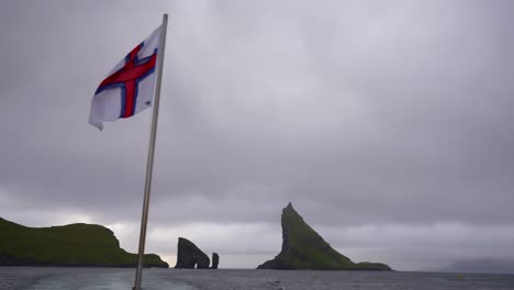 barco de las islas feroe con una bandera nacional ondeando dejando atrás pilas de mar drangarnir