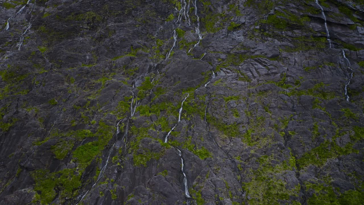 Inspiring aerial looking over rocky mountains teeming with waterfalls in Fiordland, New Zealand, South Island