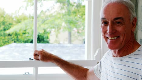 Portrait-of-smiling-senior-man-standing-next-to-window