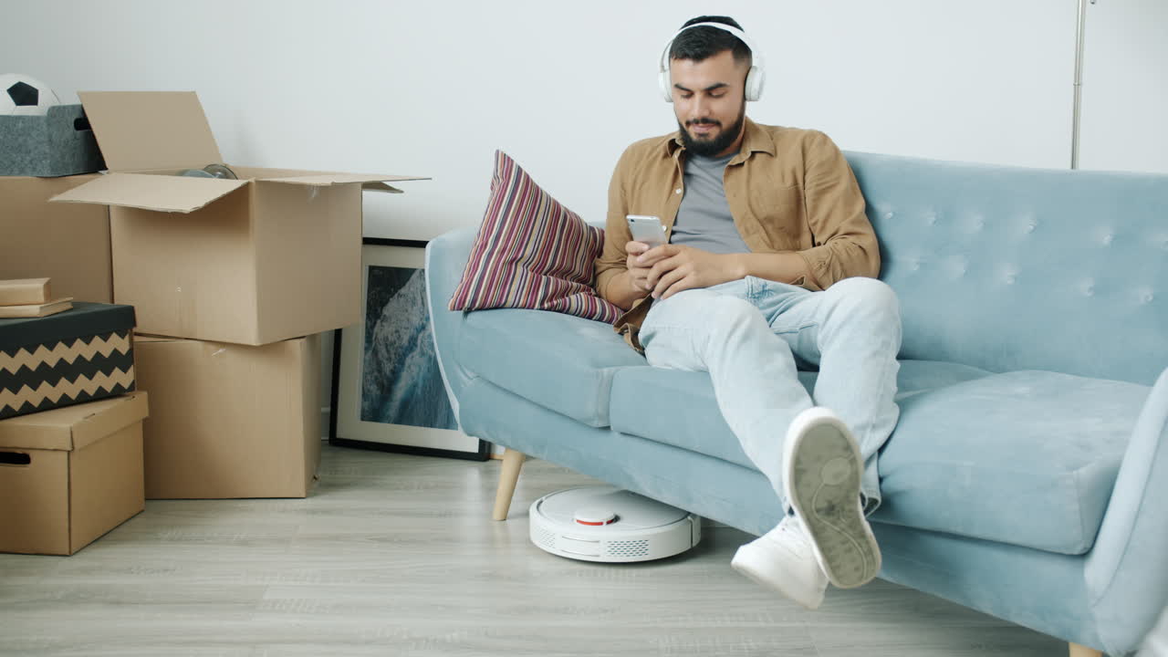 Man Relaxing on a Sofa While Robot Vacuum Cleans