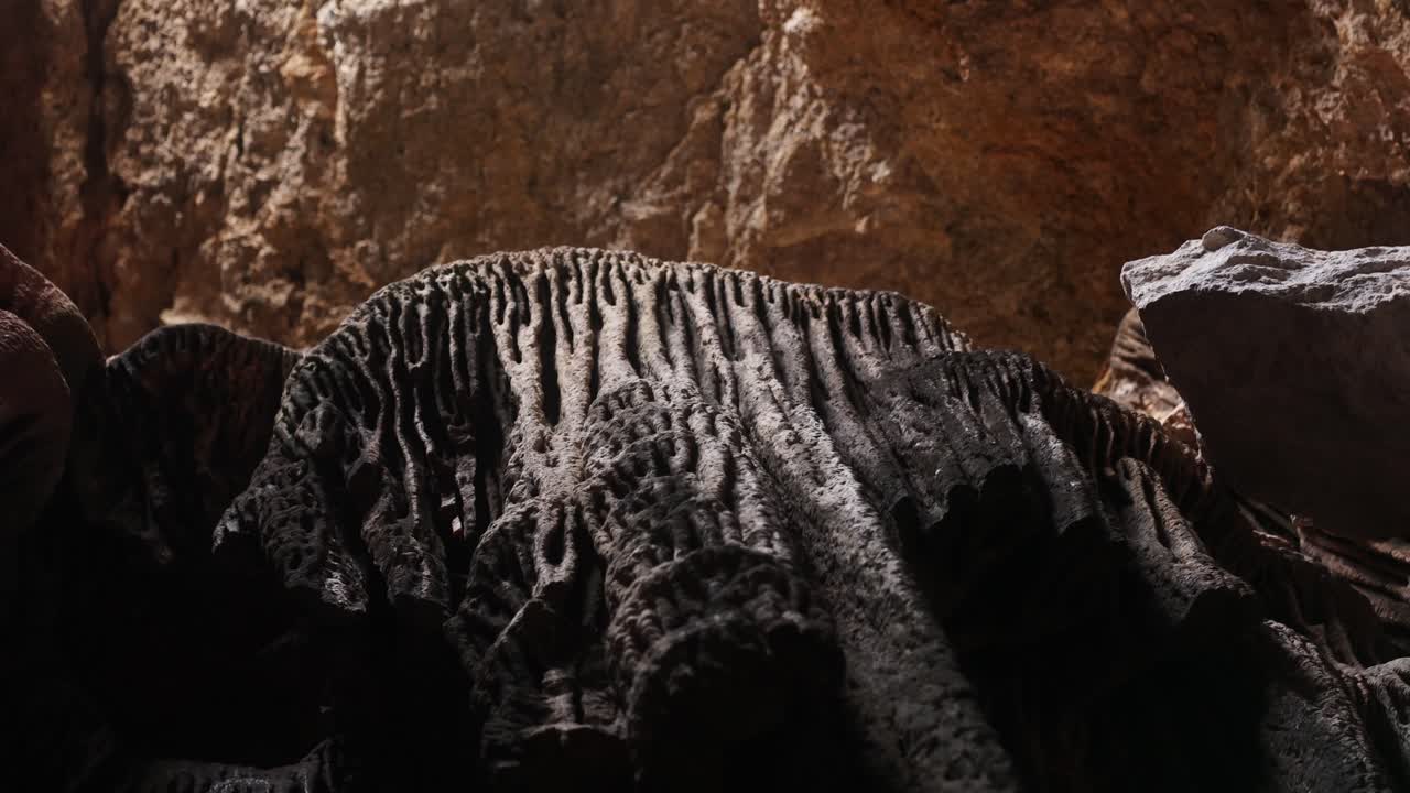 Low angle rotating view inside Ibiza limestone cave highlighting textured flowstone formations resembling organic shapes under dramatic natural light