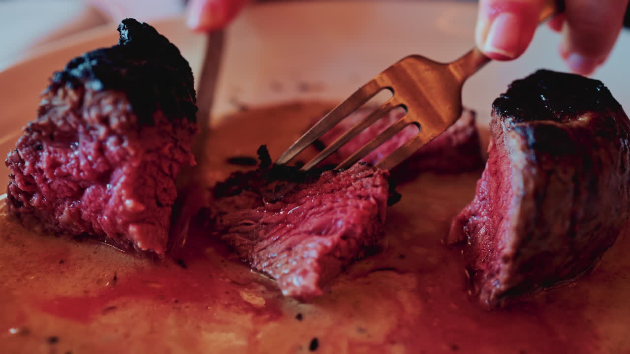 Close up of a knife slicing through a medium rare steak, exposing its tender, juicy interior