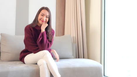 한 젊은 여성이 손에 턱을 들고 크고 편안한 소파에 다리를 꼬고 앉아 있다