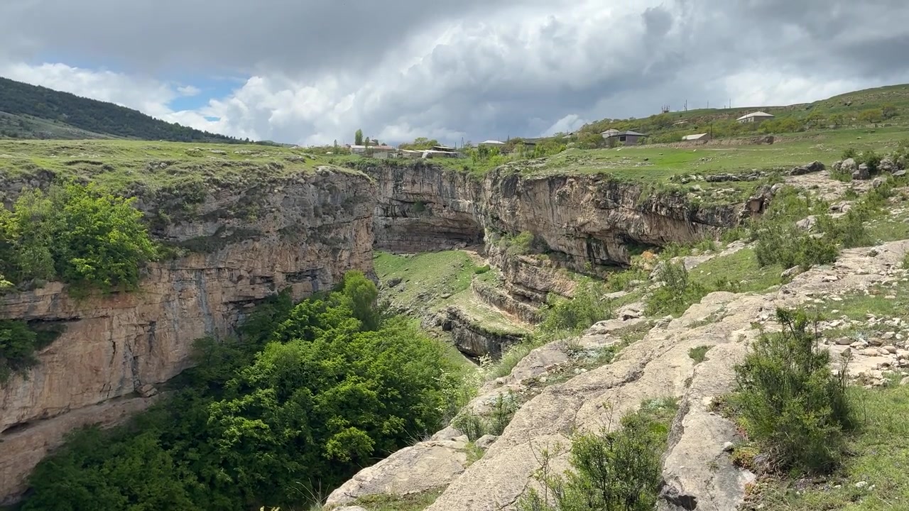 Un'inquadratura ampia cattura una profonda gola di montagna con ripide scogliere rocciose e una lussureggiante vegetazione verde sotto un cielo nuvoloso nel distretto di Gunibsky, Repubblica del Dagestan, Russia