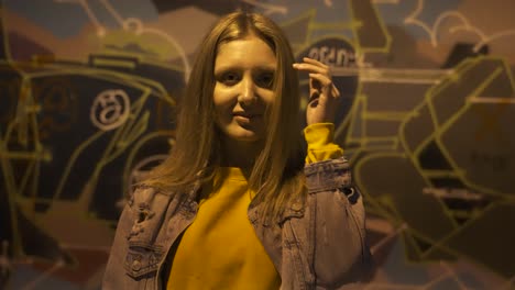 portrait of young woman posing to camera at night in front of graffiti wall slow motion