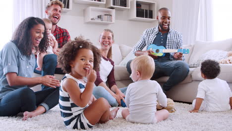 friends with toddlers playing and singing on floor and sofa