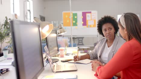 diverse business female colleagues in discussion using laptop in casual office meeting, slow motion