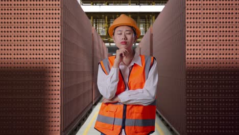 asian female engineer with safety helmet thinking and looking around then raising her index finger while standing with red brick packed in stacks are stored
