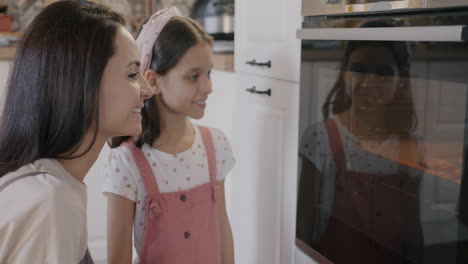 mother and daughter checking baked goods in oven
