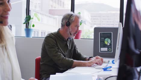 hombre de negocios caucásico sentado usando una computadora hablando por teléfono con auriculares en la oficina