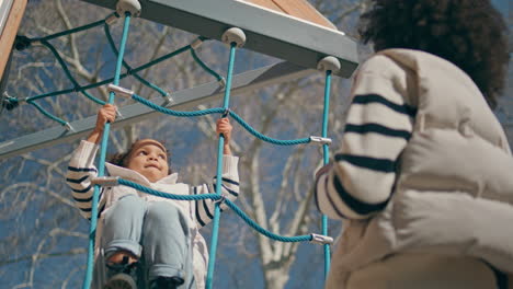 kid climbing rope ladder sunny day. little girl playing on playground