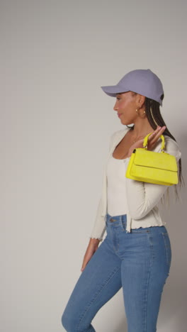 vertical video of female social media influencer producing user generated content in studio modelling yellow handbag