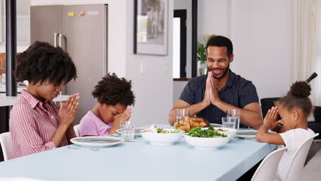 family saying grace before meal around table at home