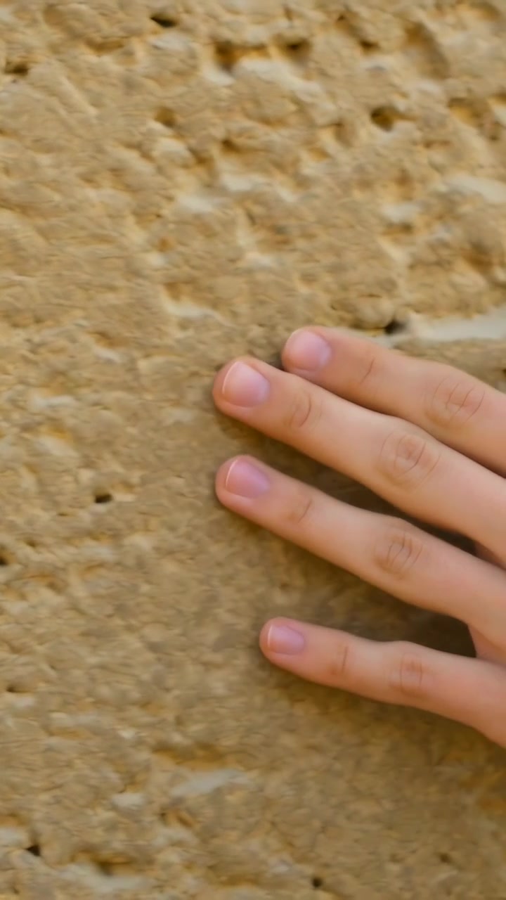 Vertical video: Entering right hand sliding fingertips on tan rock face, seeking groove, copy space