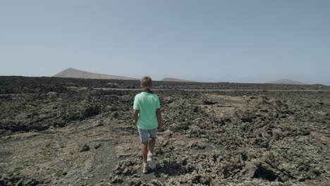 Following-a-boy-walking-across-rocky-landscape