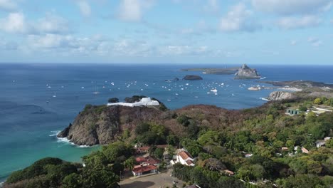 forward-movement-with-drone-on-the-island-of-Fernando-de-Noronha,-lighthouse-and-boats-in-the-background,-blue-sky-and-sunny-day,-view-of-the-fort