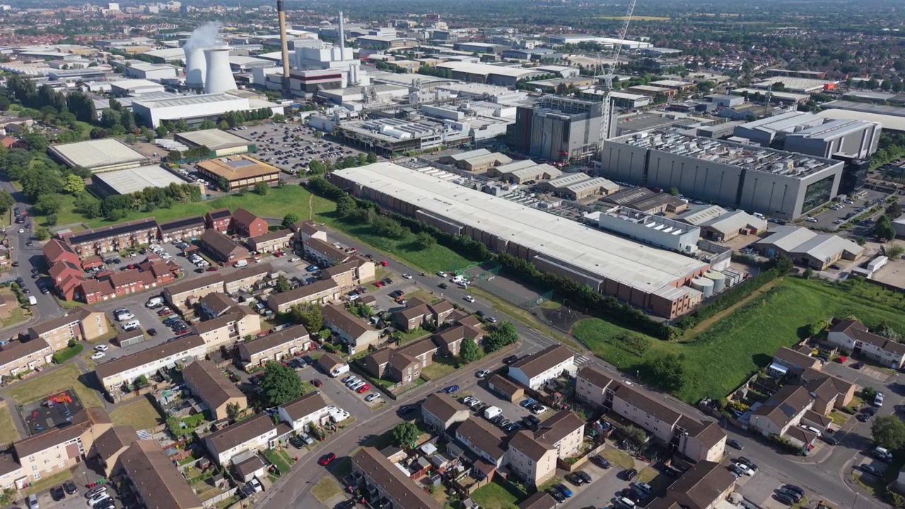 Un'ampia prospettiva aerea cattura un moderno campus di data center accanto a un'area residenziale. Il sole splendente di mezzogiorno illumina strade, auto parcheggiate e spazi verdi in quest'area a uso misto