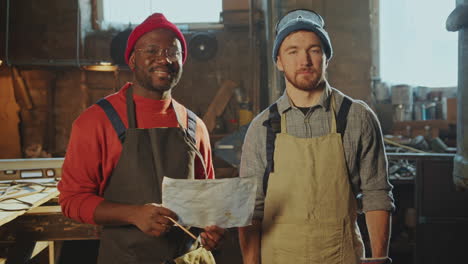 portrait of two diverse blacksmiths posing at camera in workshop