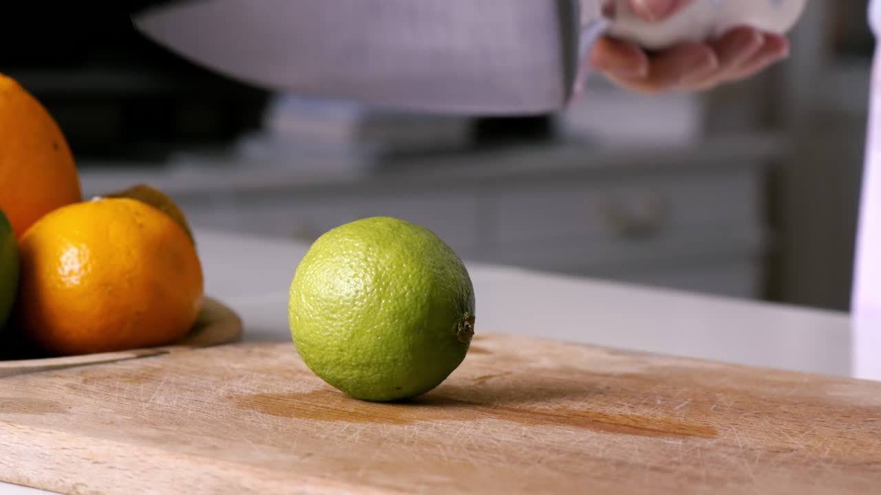 Woman slicing lime in two parts on a wooden board. Fruits on the background. Slow motion