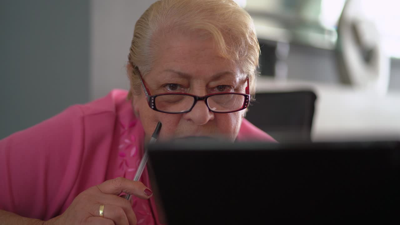Older woman with pink top and glasses looking at laptop in living room