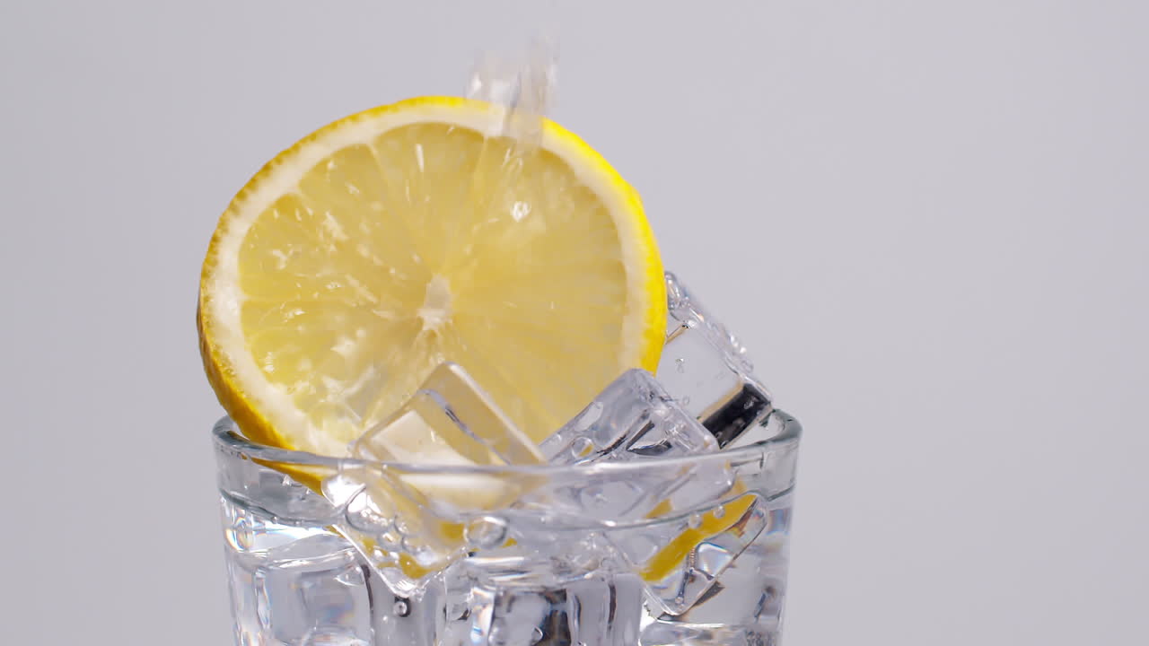 Acqua frizzante fredda e fresca che si versa in un bicchiere con ghiaccio e fette di limone