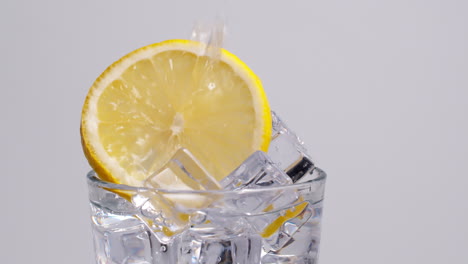 Cold-fresh-sparkling-water-pouring-into-a-glass-with-ice-and-lemon-slices