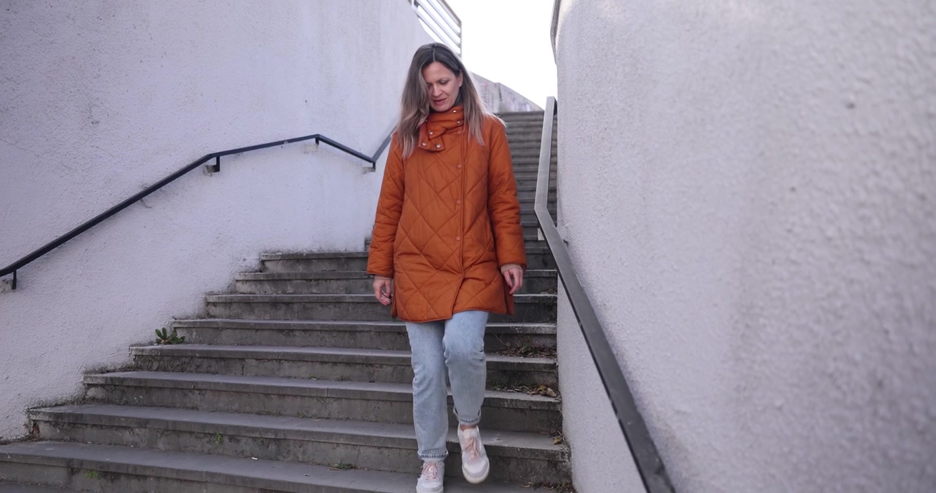 Donna bionda con cappotto invernale scende di corsa le scale della metropolitana