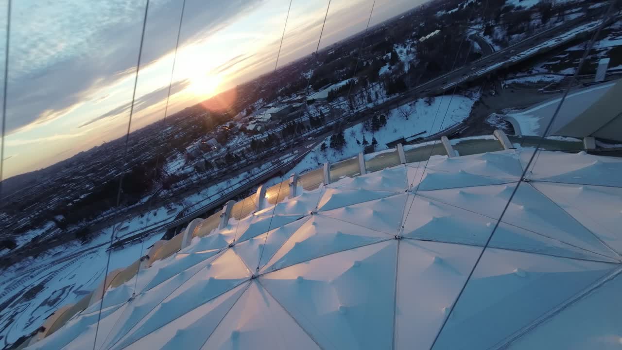 FPV drone flies over Montreal Olympic Stadium at sunset, snowy roof glistening in winter light
