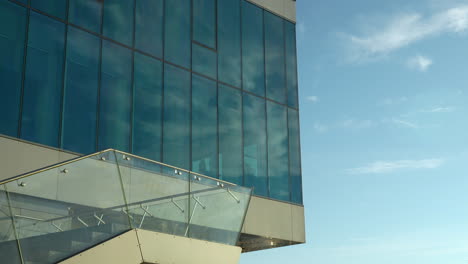 Fachada-Reflectante-Del-Edificio-Bajo-Un-Cielo-Despejado-Con-Una-Moderna-Barandilla-De-Cristal-En-Primer-Plano