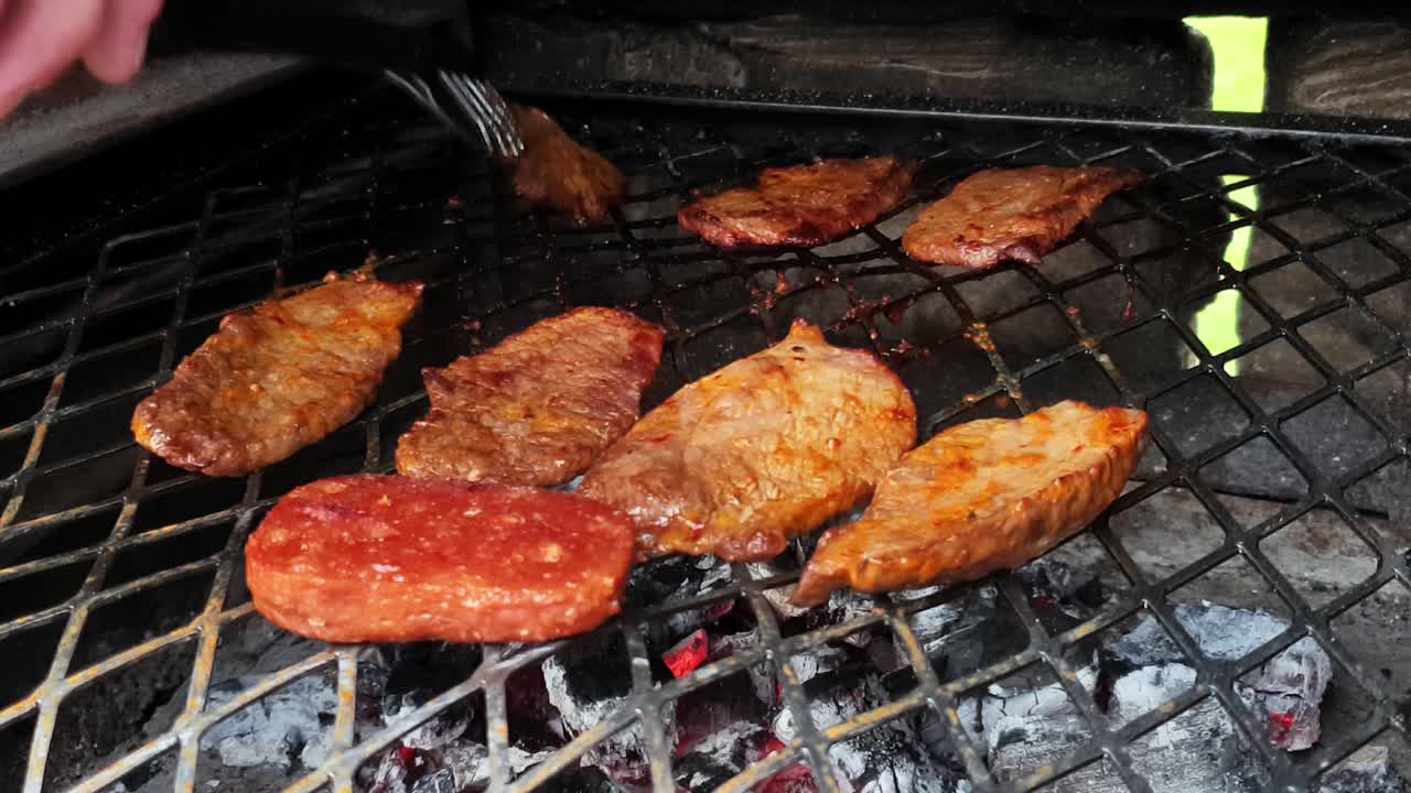 Barbecue bbq steel Grill tenderized beef steak pieces being turned over to the other side over white hot coals slowly frying the meat to perfection.
