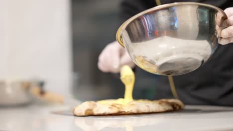 cocinero irreconocible extendiendo queso derretido en la base de la pizza horneada en la cocina. manos masculinas engrasando ingrediente para una deliciosa comida en la pizzería del restaurante. concepto culinario y de cocina