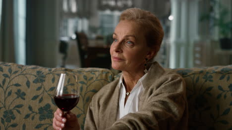 portrait pensive elderly woman enjoying red wine glass at home. old aged lady