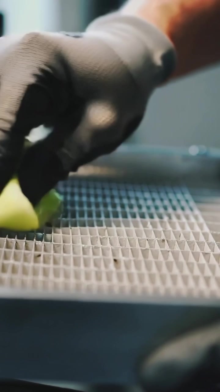 Vertical video: Placing gloved hand pressing triangle sponge over honeycomb grid at bench, cleaning
