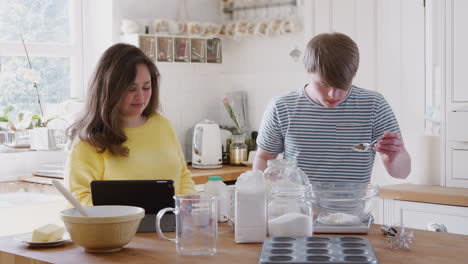 young downs syndrome couple following recipe on digital tablet to bake cake in kitchen at home