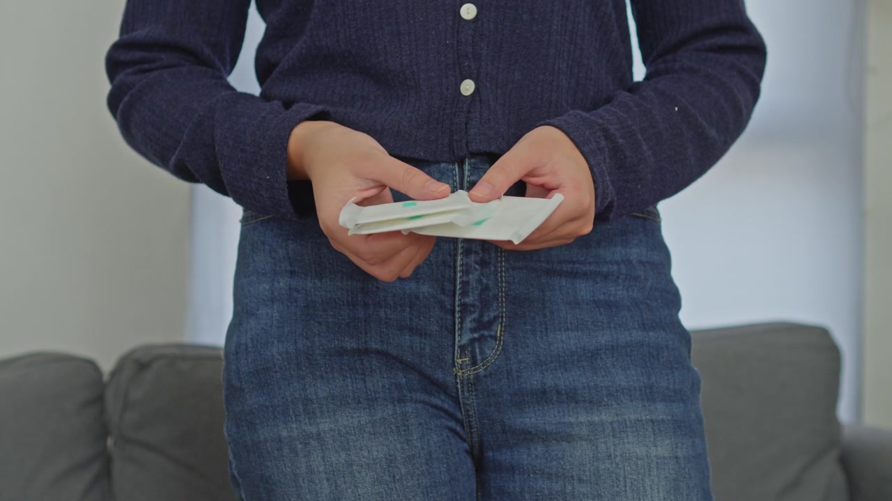 Close-up van een vrouw in jeans die meerdere verpakte maandverbanden voor menstruatiezorg vasthoudt.