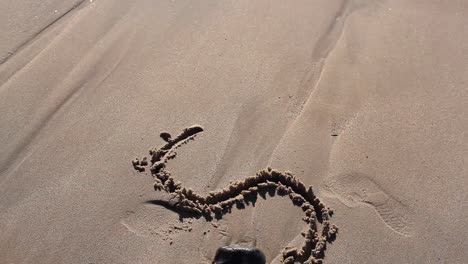 girl is drawing on a beach in the sand letter s. it is a sunny day. camera is directed downwards. girls hair are swaying in front of camera. filmed in hd