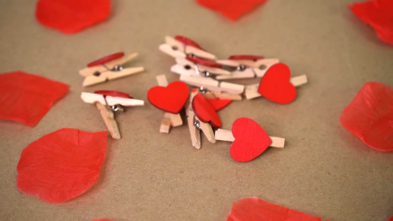 Pequenos prendedores de madeira com mini corações entre pétalas de rosas vermelhas espalhadas.