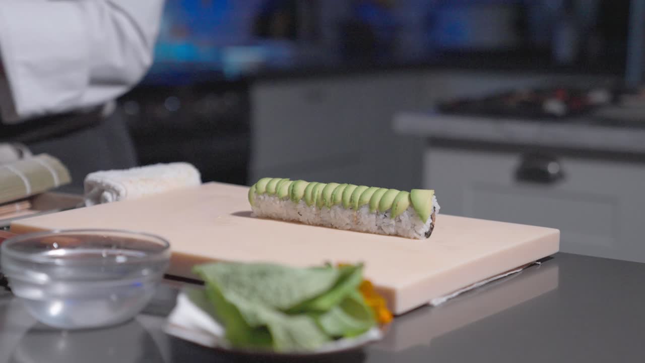A rising shot showcases a finished sushi roll topped with fresh avocado, highlighting its vibrant colors and presentation. Perfect for sushi, culinary, and food styling content.