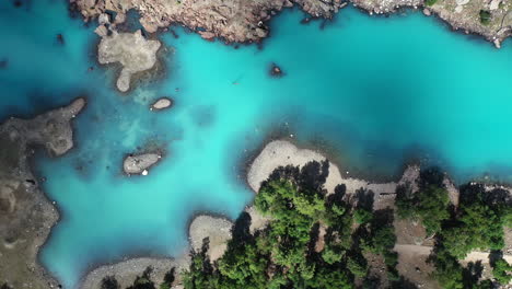 cinematic drone shot of turquoise colored water in the mountains at naltar valley in pakistan, slowly descending and rotating aerial shot