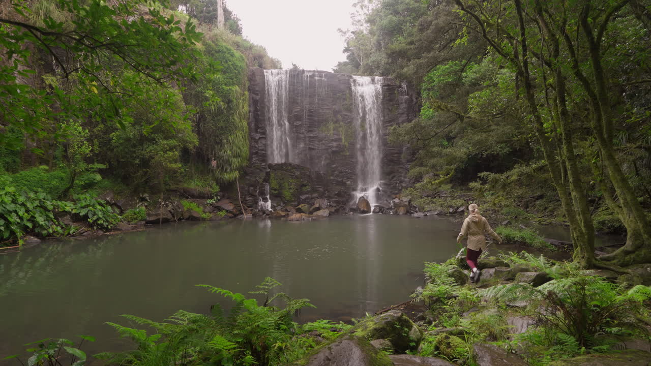 mujer llegando a una cascada de gemas escondidas rodeada de exuberante selva tropical, mujer explorando la naturaleza de nueva zelanda