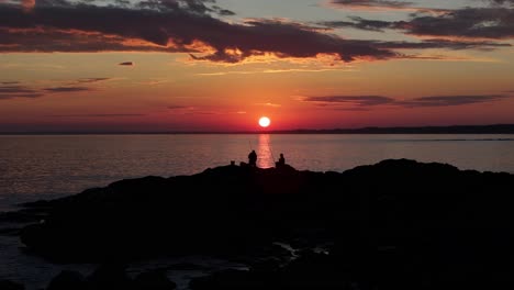 drone orbits fishermen on rocks during a magical sunset at the coast of uruguay. the sun glows before setting, reflecting over the water. sky and clouds painted in warm colors