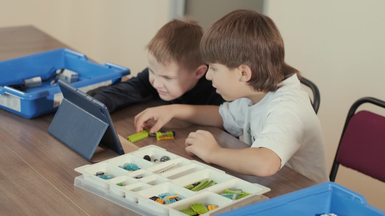 dos niños pequeños se centraron atentamente en ensamblar piezas de un kit de robótica, con una tableta que mostraba instrucciones, promoviendo el aprendizaje y la creatividad.