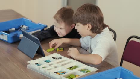 two young children intently focused on assembling parts from a robotics kit, with a tablet displaying instructions, promoting stem learning and creativity.