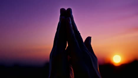 silhouetted hands form a heart shape around the setting sun against a vibrant sunset horizon, creating a peaceful and warm ambiance