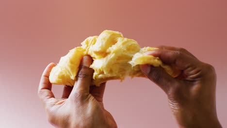 video of close up of hands with croissant on beige background