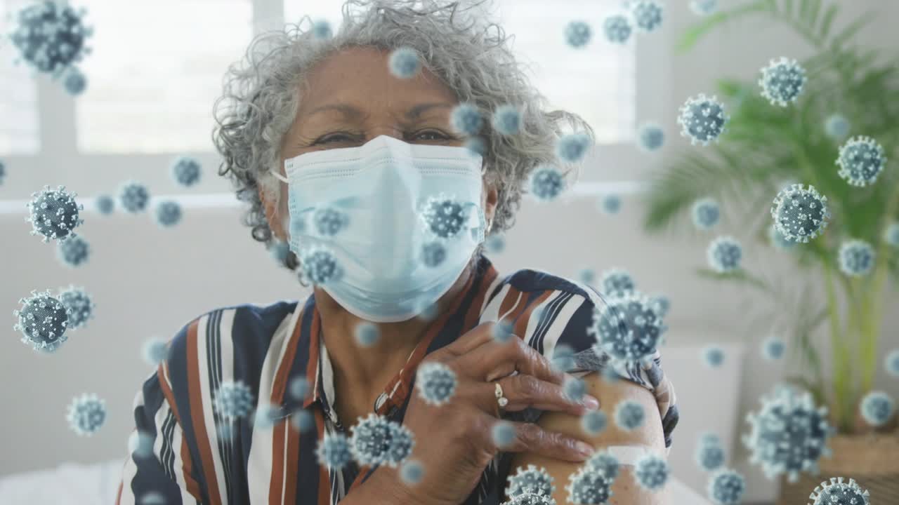 Senior masked woman rubbing arm for relief after jab at home, viral particles drifting around her