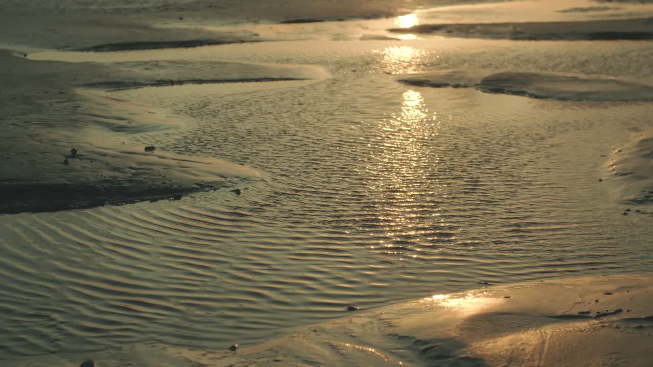 Ripples and sunset reflection in golden light on sandy tidal flats, tranquil water texture, peaceful atmosphere and natural warm scene