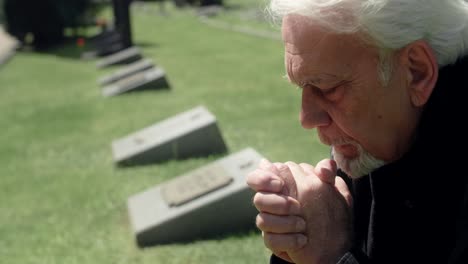 elderly man praying at cemetery